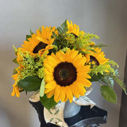 Bouquet of yellow sunflowers in a ribbed metal container with a ribbon