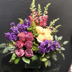 Bouquet of pink and peach roses with purple flowers in a glass vase