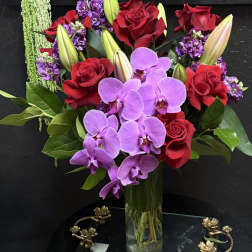 Bouquet of red roses, purple orchids, and lilies in a glass vase