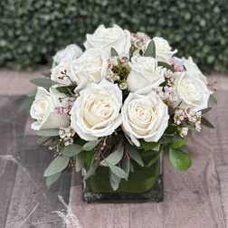White rose bouquet in a square glass vase with small pink blossoms