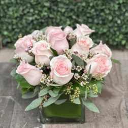 Pink roses arranged in a square glass vase with small white filler flowers