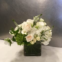 White floral arrangement in a square glass vase with roses and hydrangeas