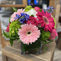Mixed bouquet with pink gerbera daisies, roses, and blue flowers in a glass vase