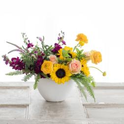 Mixed bouquet in a white vase with sunflowers, roses, and orange blooms