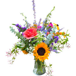 Mixed bouquet in a clear glass vase with sunflowers, a coral rose, and purple blooms