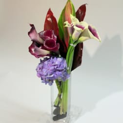 Purple calla lilies and a lavender hydrangea in a clear glass vase