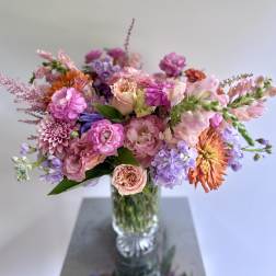 Mixed pink, peach, purple, and orange flowers in a clear glass vase
