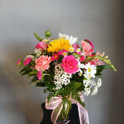Mixed bouquet of pink, white, and yellow flowers in a glass vase with a pink ribbon