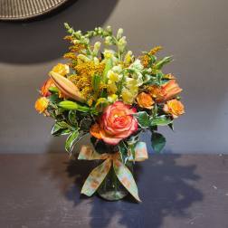 Bouquet of orange and pink roses with lilies in a glass vase
