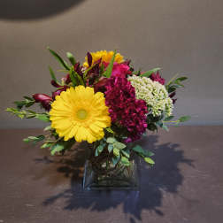 Mixed bouquet in a square glass vase with yellow daisies and magenta blooms