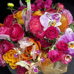 Bright mixed bouquet of pink roses, orchids, and orange blooms in brown wrap