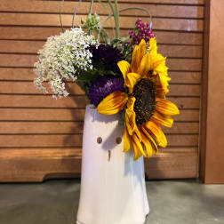 Sunflowers and purple flowers arranged in a white ceramic vase
