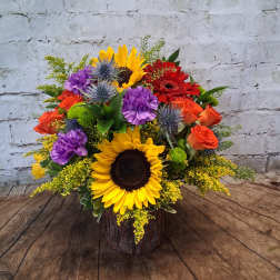 Colorful bouquet with sunflowers, roses, and purple blooms in a rustic wood container