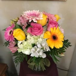 Pink and yellow roses with gerbera daisies in a glass vase