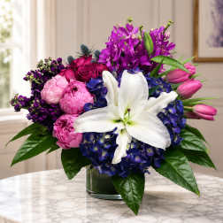 Colorful bouquet with white lily, pink peonies, and purple flowers in a glass vase