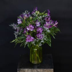 Purple alstroemeria bouquet in a green glass jar vase