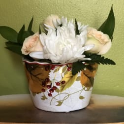 White and peach flowers arranged in a decorative autumn container