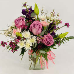 Pink roses and mixed flowers in a clear glass vase with a pink ribbon