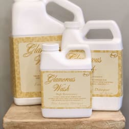 Three white laundry detergent jugs with gold labels stacked on a decorative pedestal.