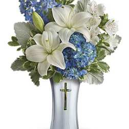 White lilies and blue flowers arranged in a silver vase with a cross