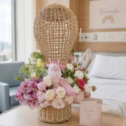 Pink and white floral arrangement with a plush giraffe in a wicker basket