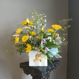 Yellow mixed bouquet in a white baby-themed vase with a ribbon