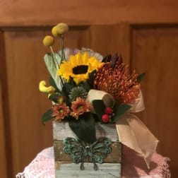 Small floral arrangement in a rustic wooden box with a sunflower and orange blooms