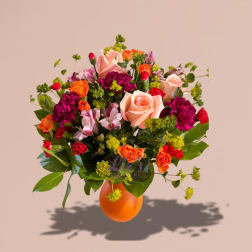 Mixed bouquet of roses, carnations, and alstroemeria in an orange vase