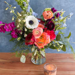Mixed bouquet in a clear glass vase with pink, orange, white, and blue blooms