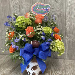 Football-themed bouquet with orange roses, green hydrangeas, and a blue bow in a sports container.