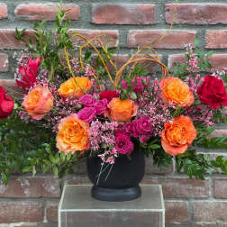 Arrangement of orange, pink, and red roses in a black vase