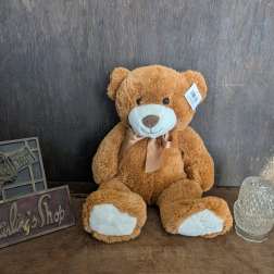 Brown teddy bear with a ribbon sitting beside a glass candle holder