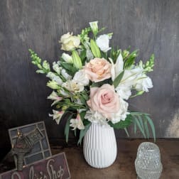 Blush roses and white lilies arranged in a white vase