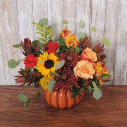 Autumn floral arrangement in an orange pumpkin vase with sunflowers and roses