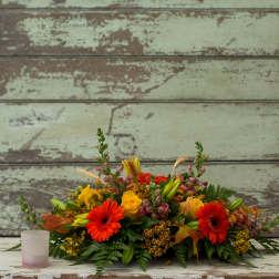 Low floral centerpiece with red gerbera daisies and yellow roses in a glass container