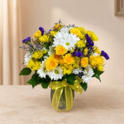 Bouquet of yellow, white, and purple flowers in a glass vase with a yellow ribbon