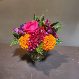 Bright mixed bouquet in a clear glass vase with pink, purple, and orange flowers.