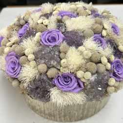 Purple roses arranged with dried beige accents in a round box