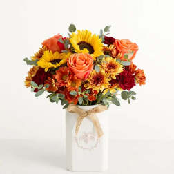 Bouquet of sunflowers, roses, and mums in a white vase with a ribbon