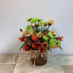 Mixed orange and green flower arrangement in a brown vase with raffia bow