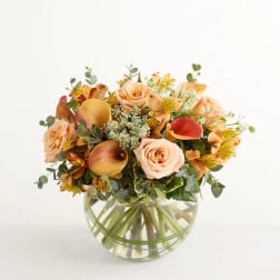 Peach and yellow flower bouquet in a round glass vase