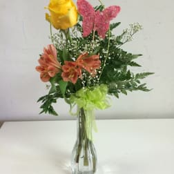 Yellow rose and orange flowers in a clear glass vase with a pink butterfly pick