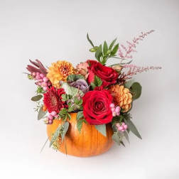 Floral arrangement in a pumpkin container with red roses and orange blooms