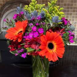 Bright mixed bouquet with orange gerbera daisies in a glass vase