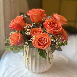 Orange roses arranged in a white ribbed vase
