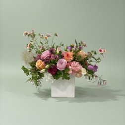Mixed pink, peach, and purple flowers in a white vase