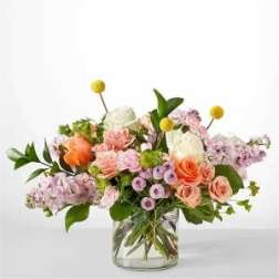 Mixed bouquet of pink, peach, and lavender flowers in a clear glass vase