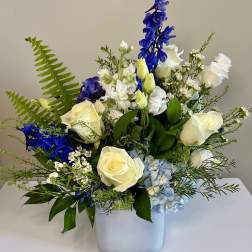White roses and blue flowers arranged in a square vase