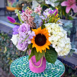 Mixed bouquet with a sunflower, lavender roses, and white hydrangeas in a pink vase