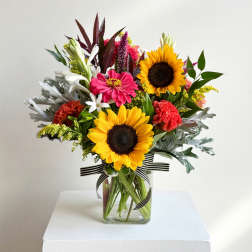Mixed bouquet with sunflowers, pink blooms, and white flowers in a glass vase